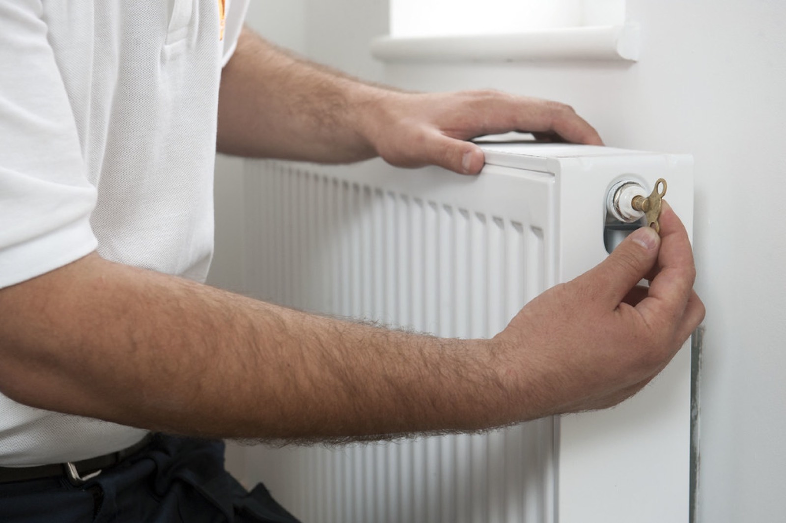 Handwerker prüft ein Thermostatventil an einem weißen Heizkörper